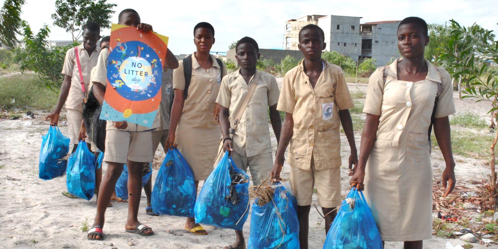 A few people standing in a row, holding plastic bags with litter. One of them is holding a poster