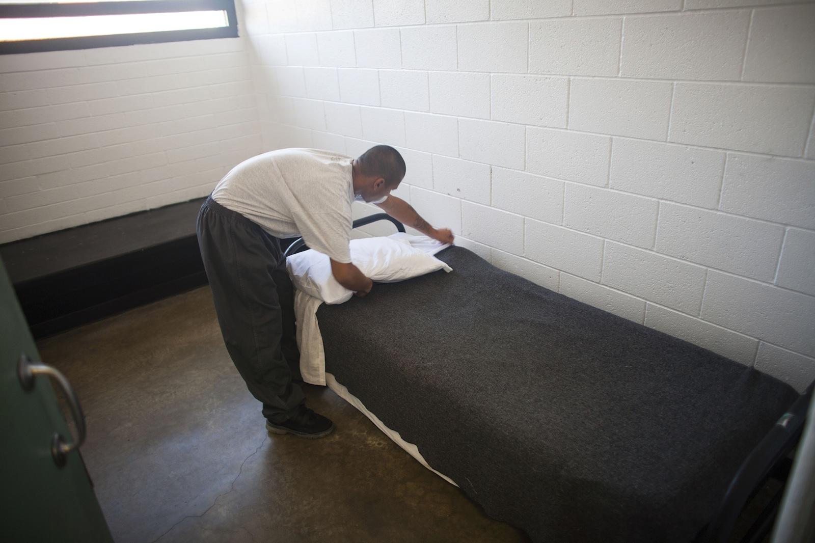 Boy making the bed in his cell. 