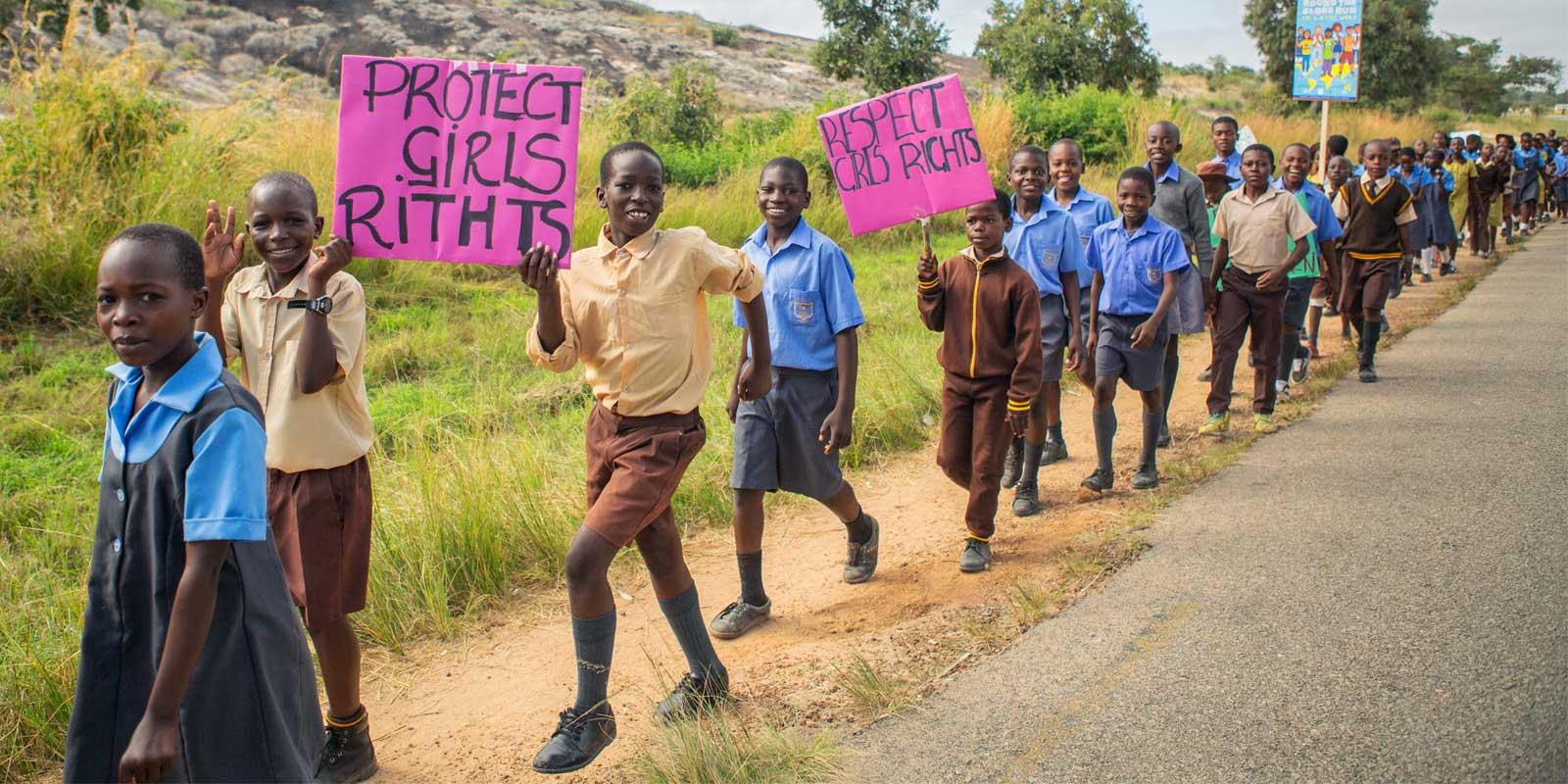 Boys walking with signs along highway in dry African  landscape. 