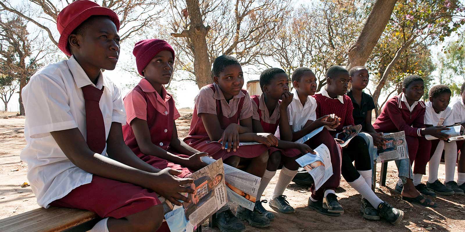 Children in schooluniforms sitting together on a low wall.