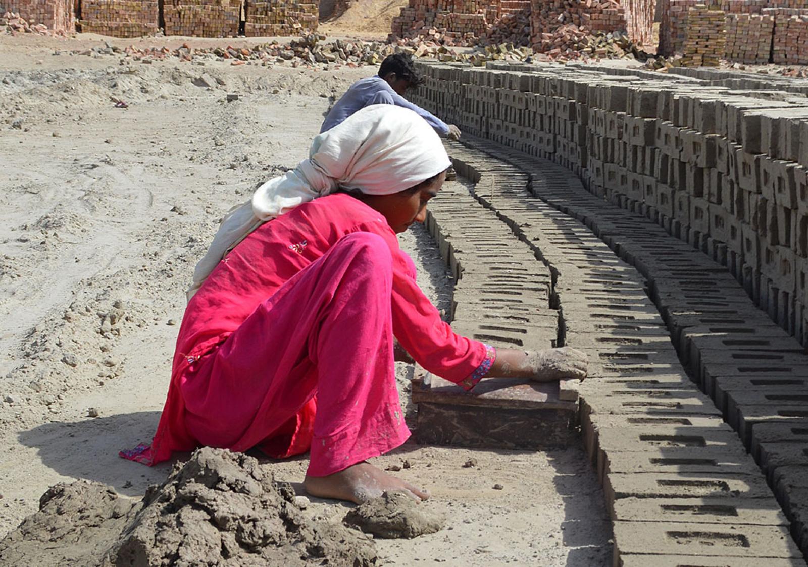 Samina sits on the ground and makes bricks