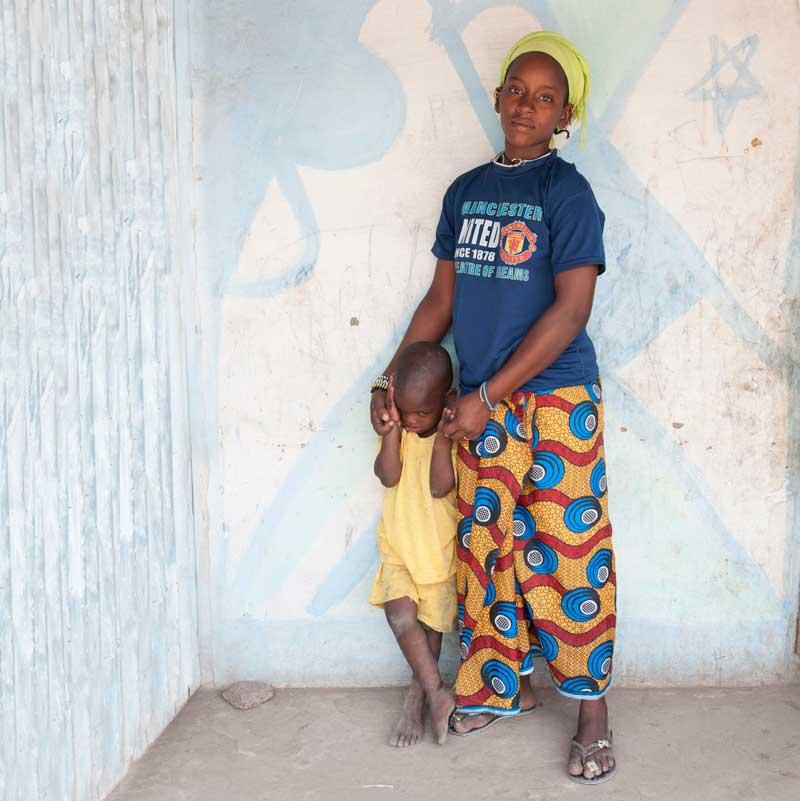 Girl standing with her child, holding his hands.