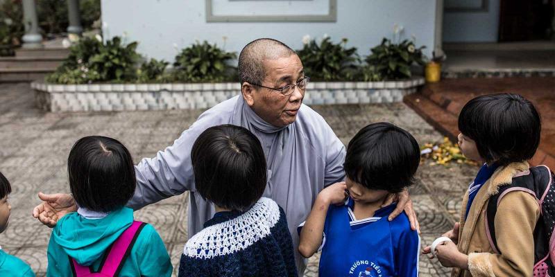 A buddhist nun has her arms around three children. 