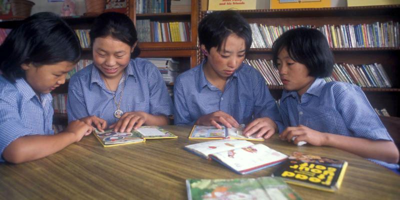 Four children in a library reading books together.
