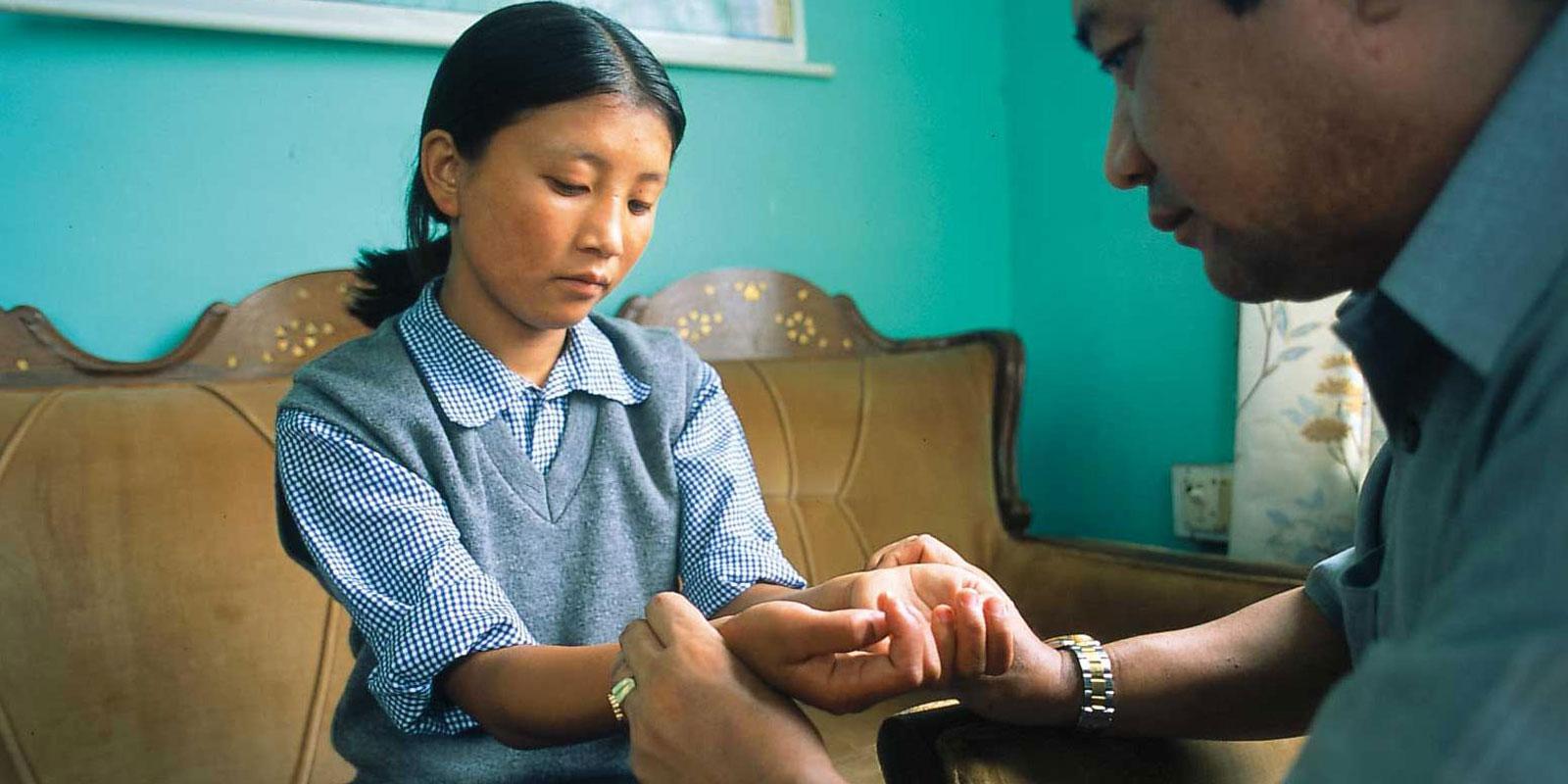Doctor feels pulse of girl in blue school uniform.