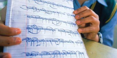 Child’s hand holding notebook with Tibetan print.