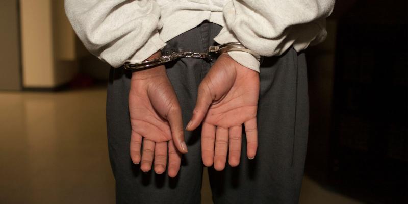 Close up of black boy with his hands behind his back in hand cuffs.